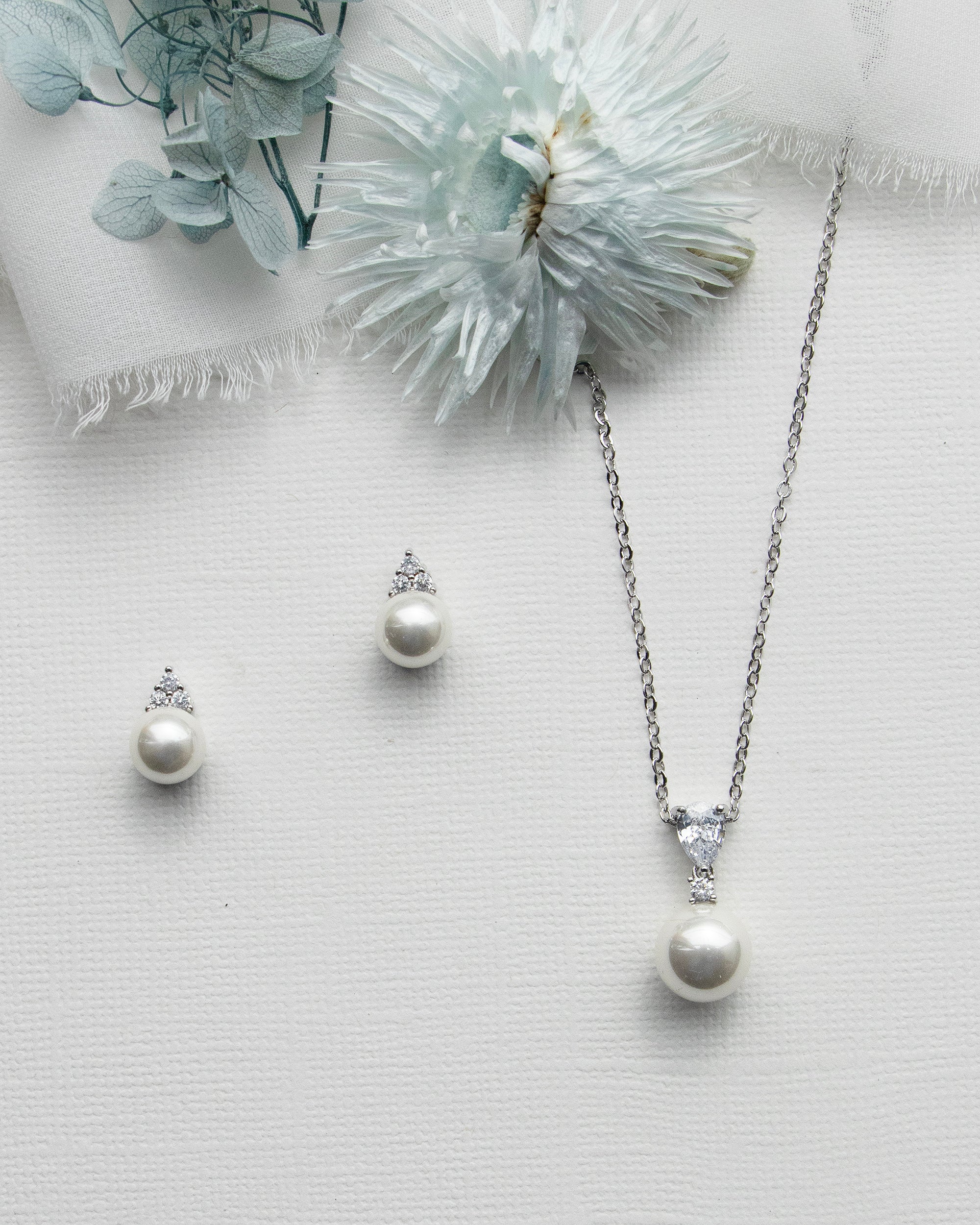 a necklace, earrings and a flower on a white surface