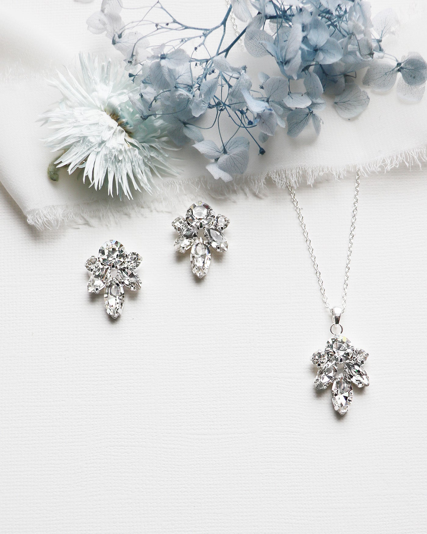 a necklace, earrings and a flower on a white surface