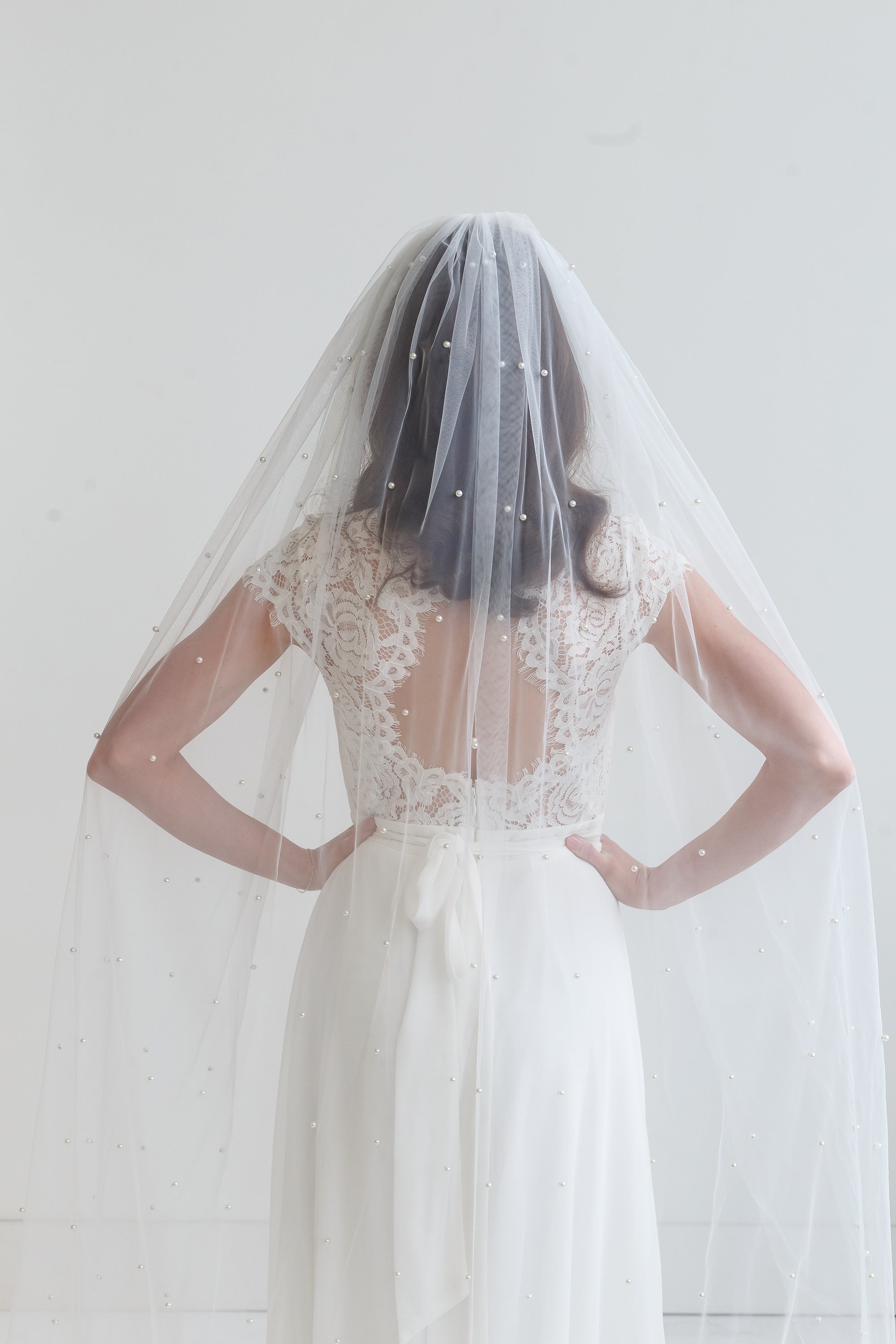 A woman wearing a white wedding dress with a veil, standing against a white background.