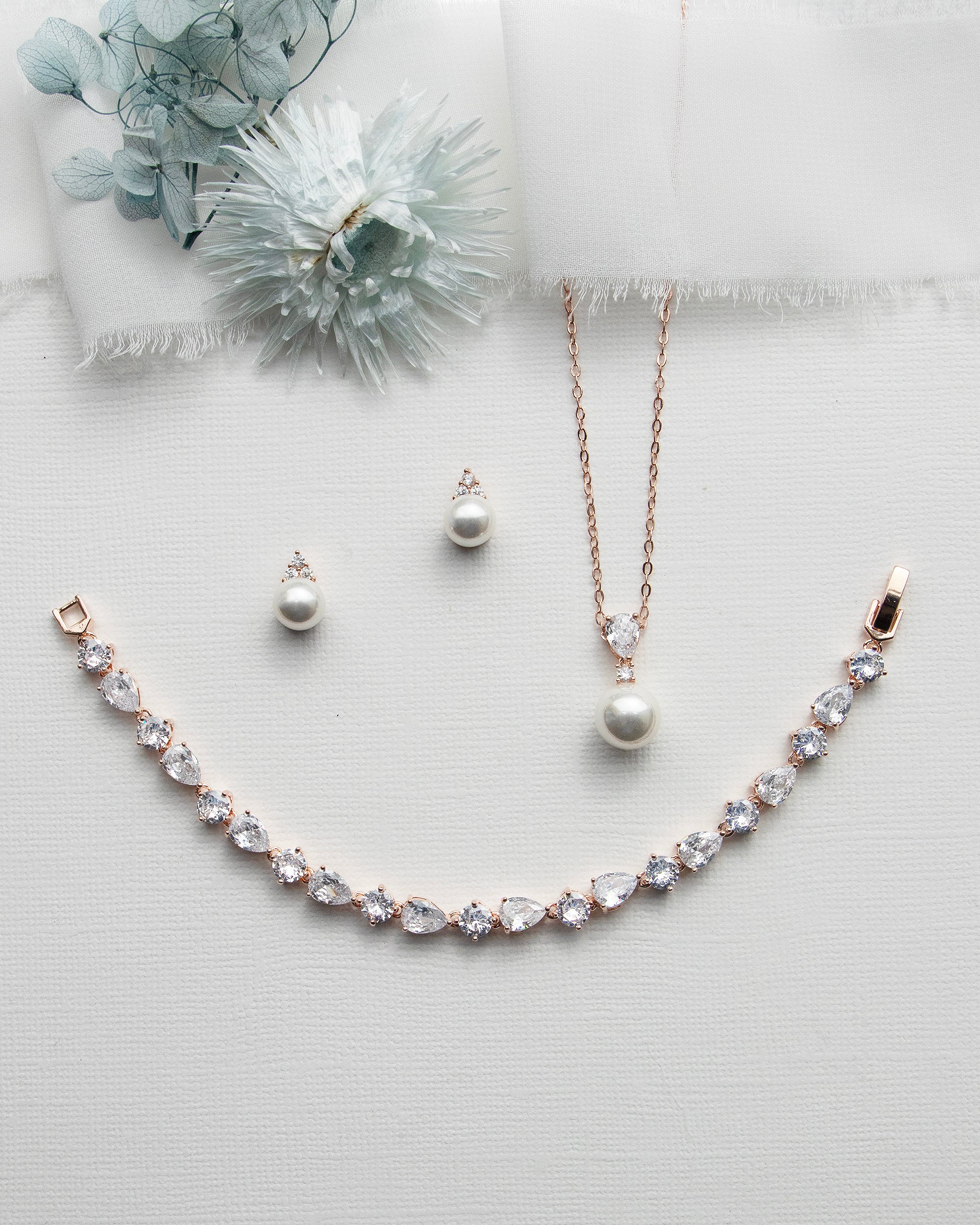 a necklace, earrings, and a flower on a white surface