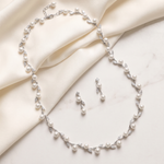 A delicate necklace and matching earrings are displayed on a white fabric surface.