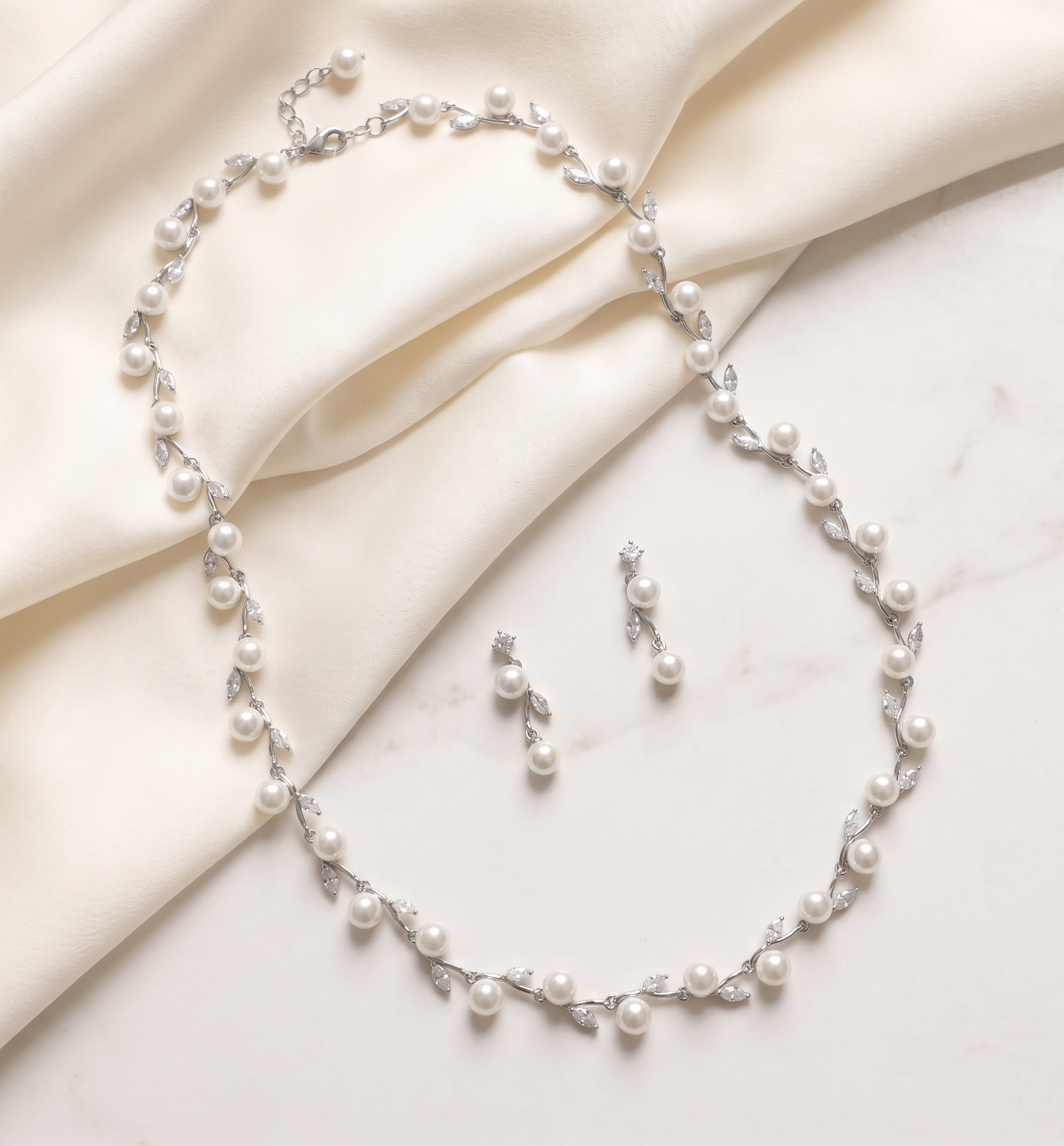A delicate necklace and matching earrings are displayed on a white fabric surface.