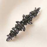 A decorative hair clip with a floral design and numerous small black gemstones.