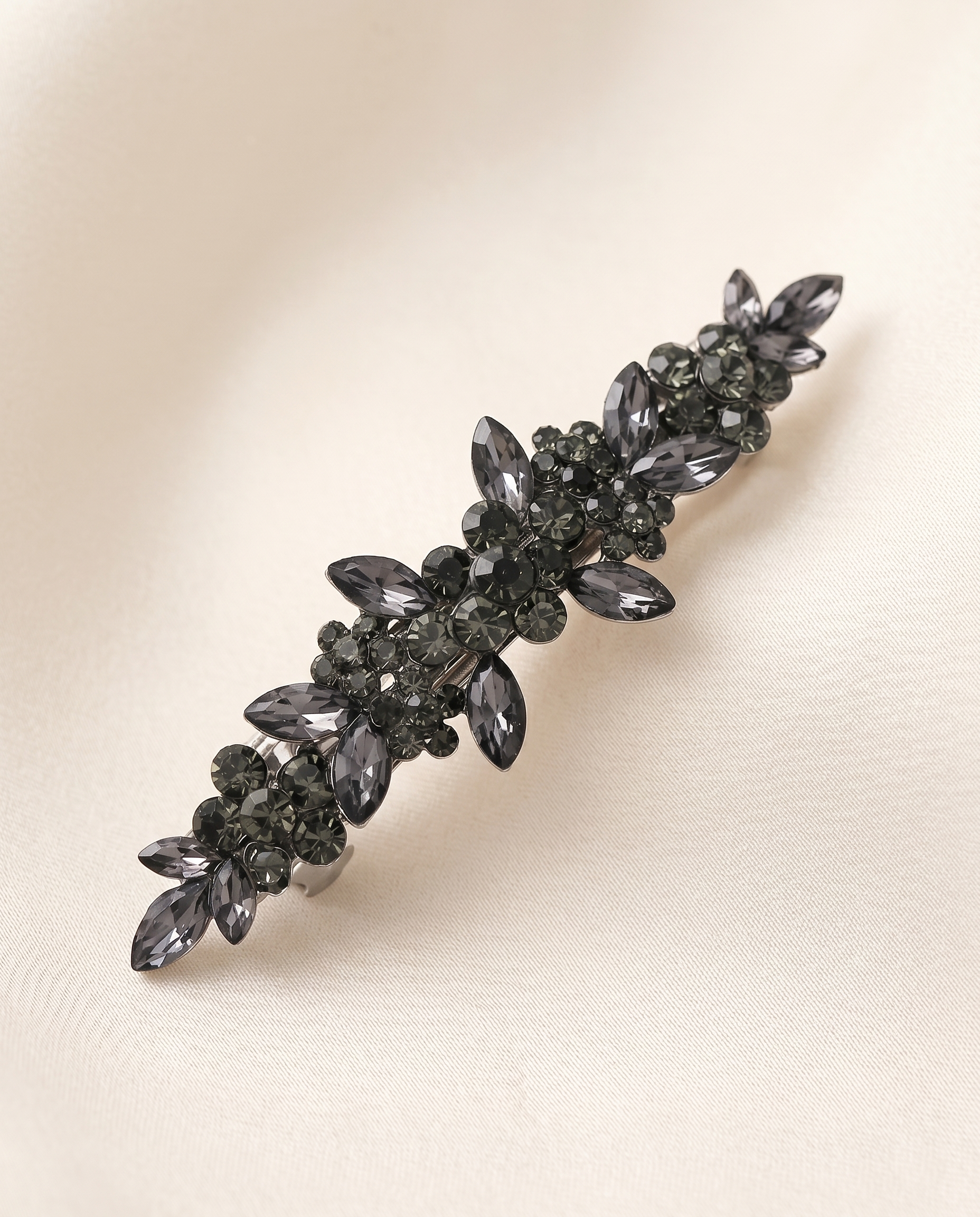 A decorative hair clip with a floral design and numerous small black gemstones.