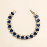 A gold bracelet adorned with blue and white gemstones, including diamonds, is displayed against a light background.