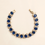 A gold bracelet adorned with blue and white gemstones, including diamonds, is displayed against a light background.