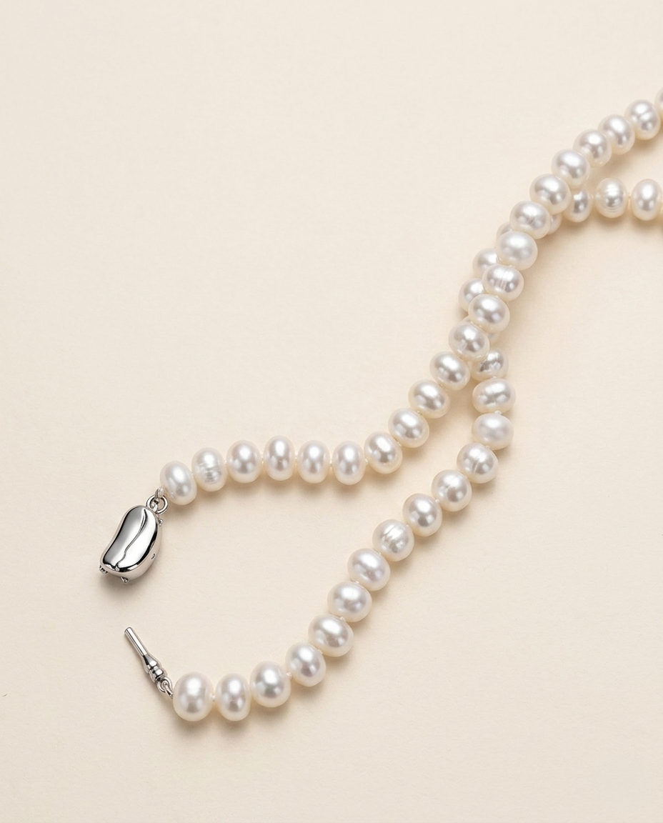 A delicate necklace made of white pearls lies on a light beige background.