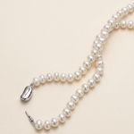A delicate necklace made of white pearls lies on a light beige background.