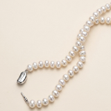 A delicate necklace made of white pearls lies on a light beige background.