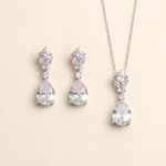 A necklace and earrings set made of white diamonds, arranged on a light beige background.