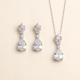 A necklace and earrings set made of white diamonds, arranged on a light beige background.