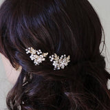 a close-up view of a person's head with dark hair styled in a half-up, half-down hairstyle. The person is wearing two decorative hair clips with small white flowers on them.