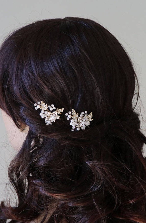 a close-up view of a person's head with dark hair styled in a half-up, half-down hairstyle. The person is wearing two decorative hair clips with small white flowers on them.