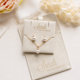 A beige jewelry box with a pearl necklace and earrings, along with a matching beige pouch, sits on a white surface. A pink flower is visible in the background, and the text "Sarah Bridesmaid" is printed on the jewelry box and pouch.