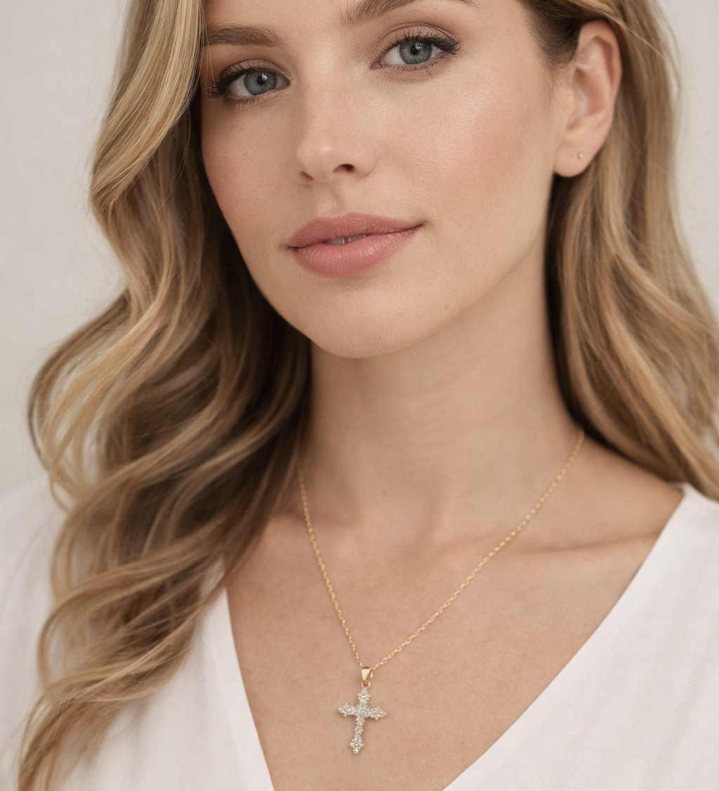 A close-up portrait of a woman with long, wavy blonde hair and a thoughtful expression, wearing a white blouse and a necklace with a cross pendant.