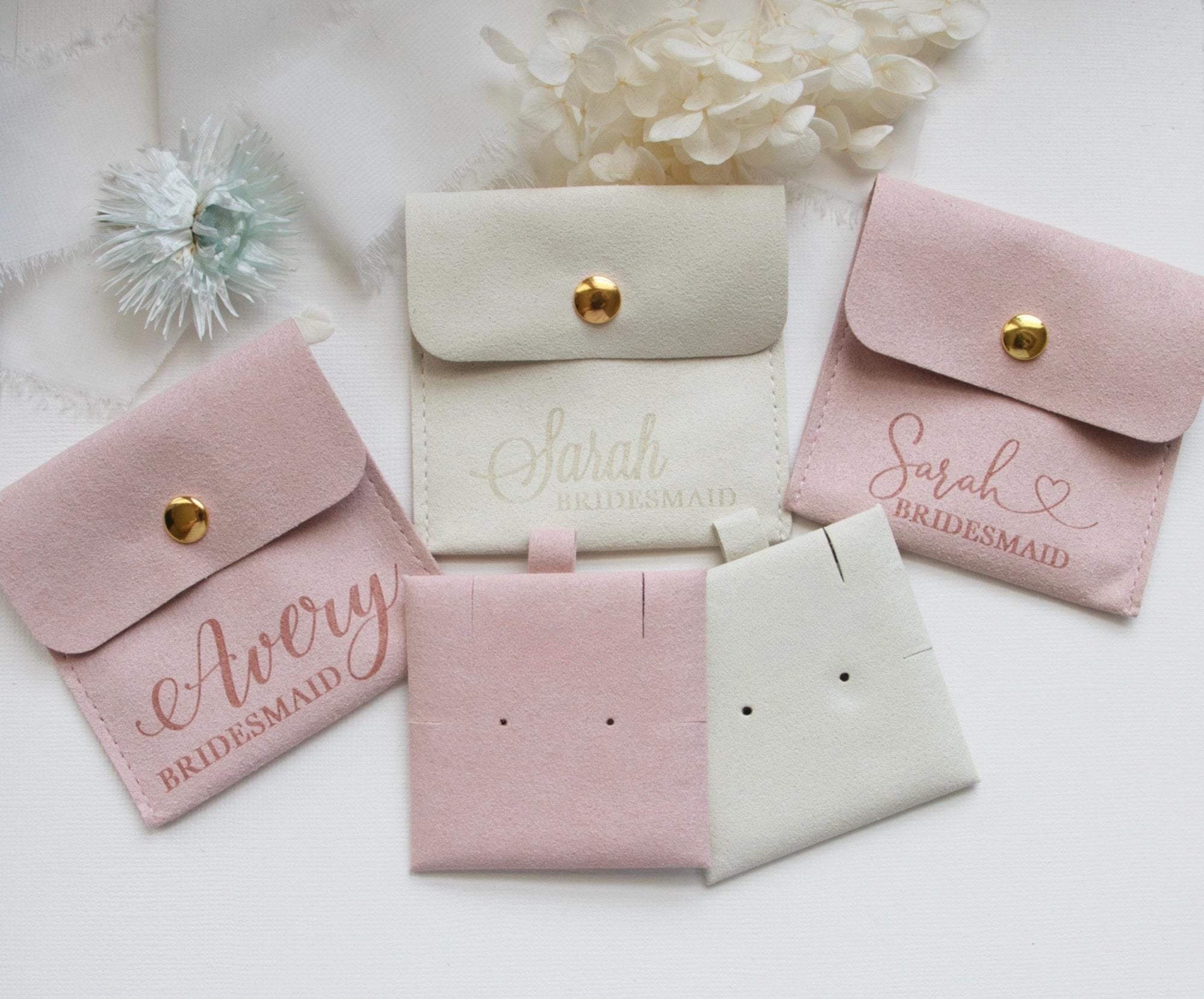 a collection of pink and white bridesmaid bags, each with a personalized name printed on it.