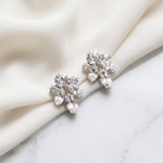 A pair of elegant diamond earrings with large, clear gemstones are displayed on a white fabric surface.