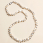 A necklace made of white pearls is displayed against a light beige background.