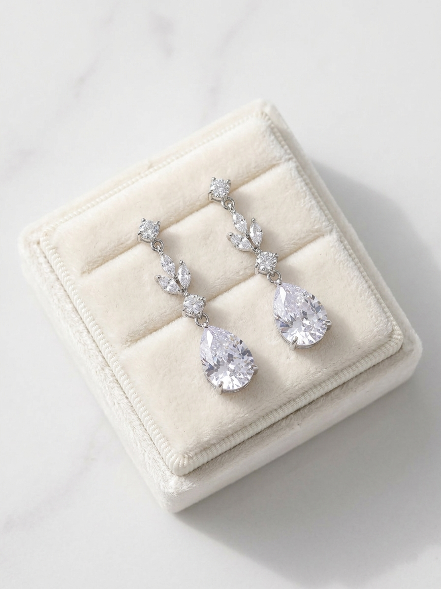 A pair of elegant earrings with large, clear gemstones, displayed in a white jewelry box on a marble surface.