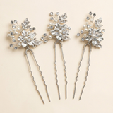 Three silver hair clips adorned with white flowers and crystals are arranged in a row against a light background.