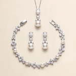 A necklace, earrings, and bracelet set made of white pearls and diamonds, arranged on a beige background.
