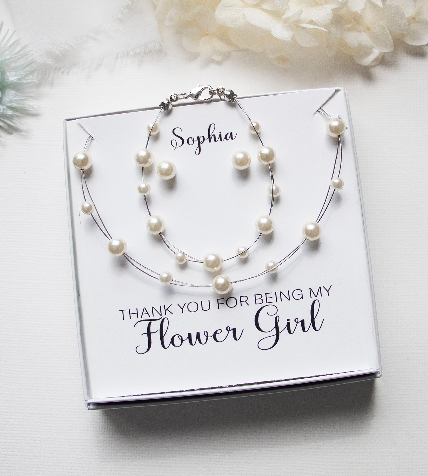 A gift box containing a necklace and bracelet with pearls, accompanied by a personalized message that says "Thank you for being my Flower Girl".