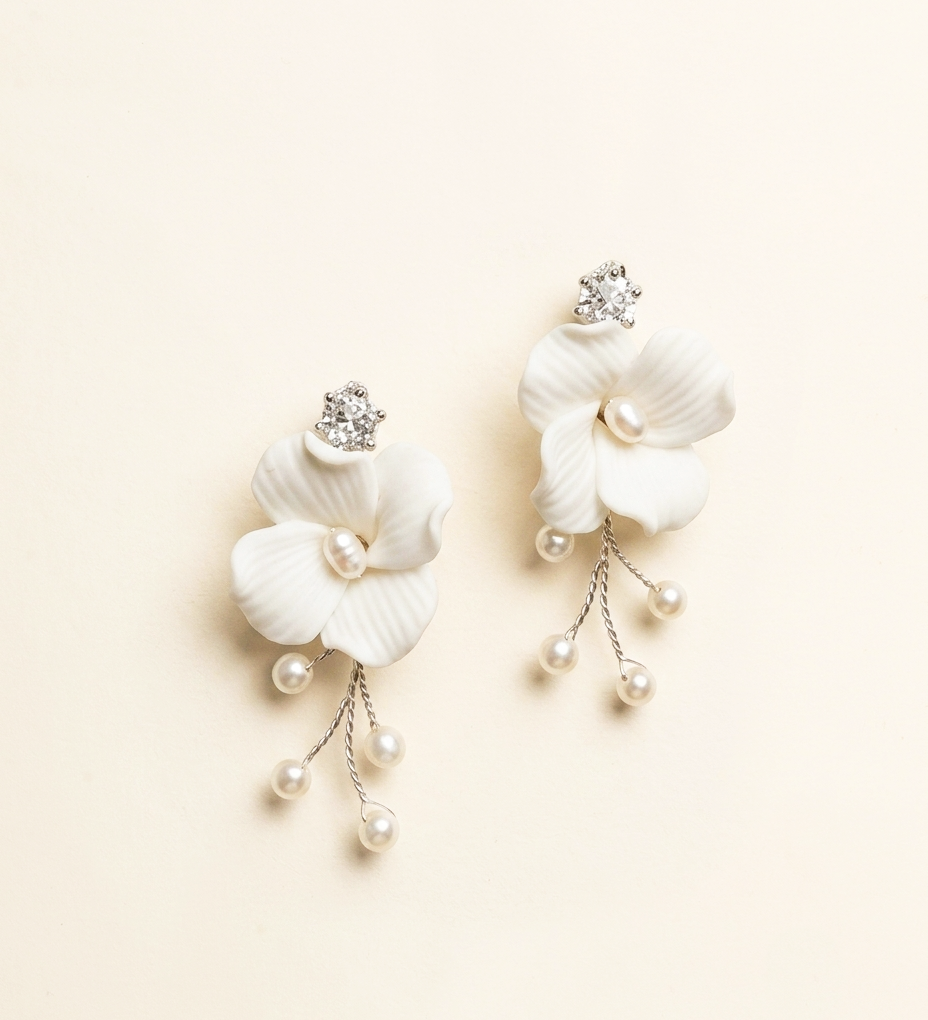 A pair of elegant white earrings with delicate flower-like designs and dangling pearls.