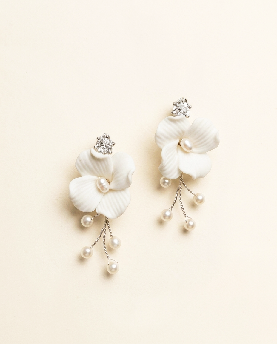A pair of elegant white earrings with delicate flower-like designs and dangling pearls.