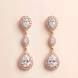 A pair of elegant earrings with a delicate design, featuring three large pear-shaped diamonds set in a halo of smaller diamonds, all encased in a rose gold-colored metal.