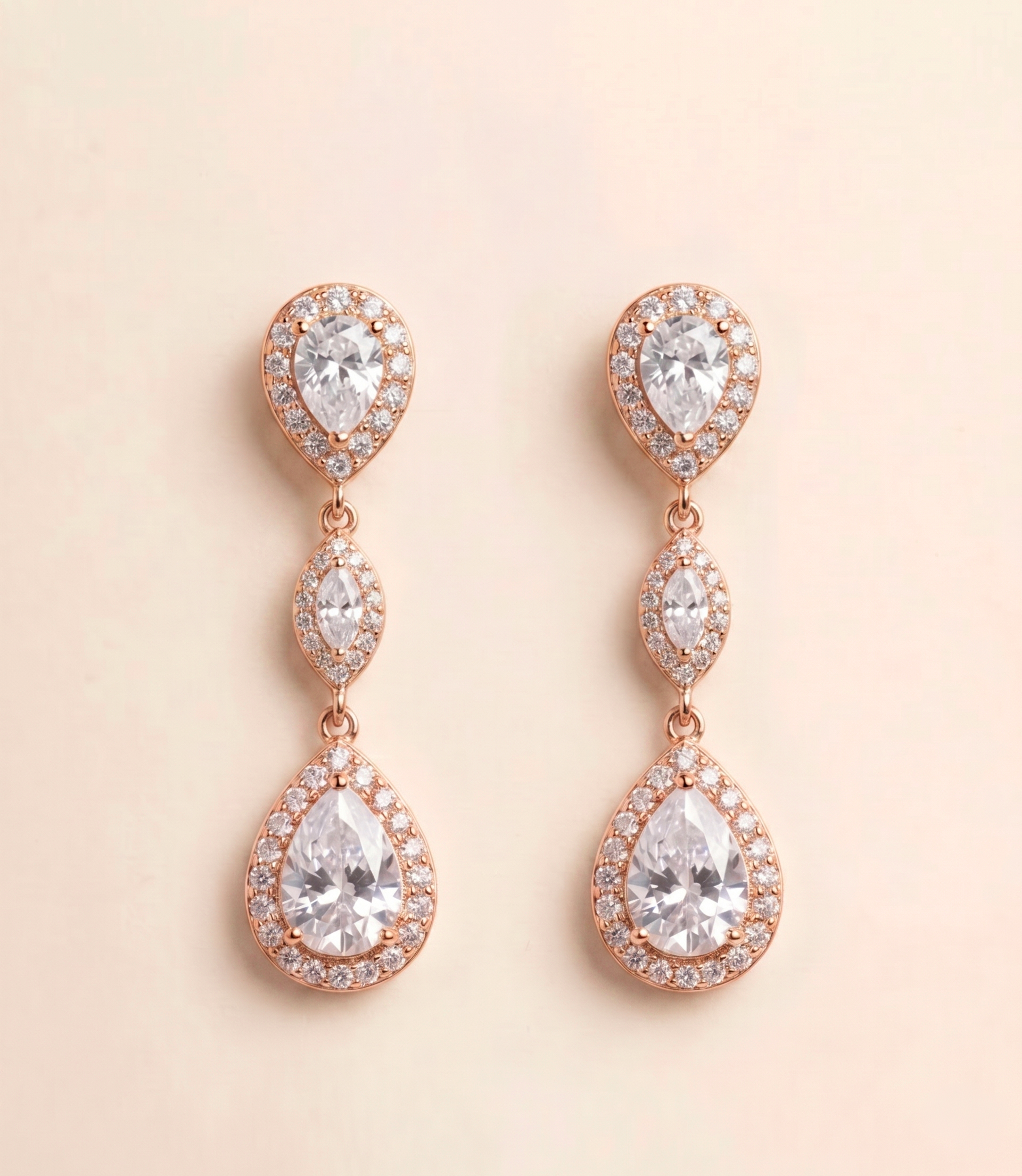 A pair of elegant earrings with a delicate design, featuring three large pear-shaped diamonds set in a halo of smaller diamonds, all encased in a rose gold-colored metal.