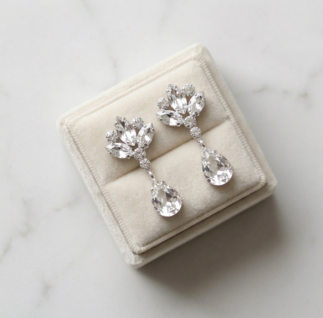 A pair of elegant diamond earrings displayed in a white velvet box on a marble surface.