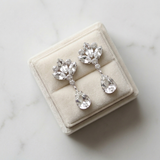 A pair of elegant diamond earrings displayed in a white velvet box on a marble surface.