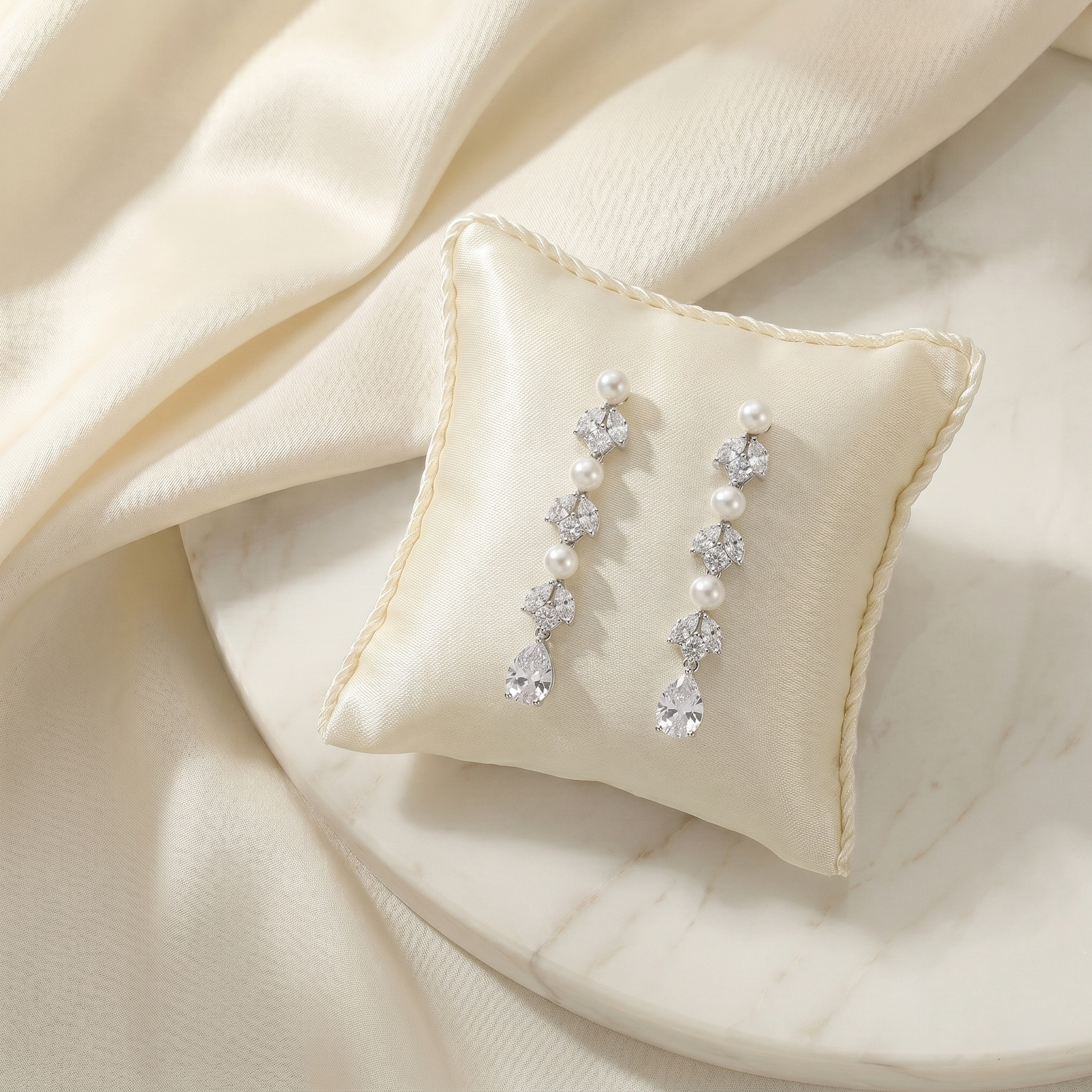 A pair of elegant earrings with pearls and clear gemstones, displayed on a white pillow or cushion.