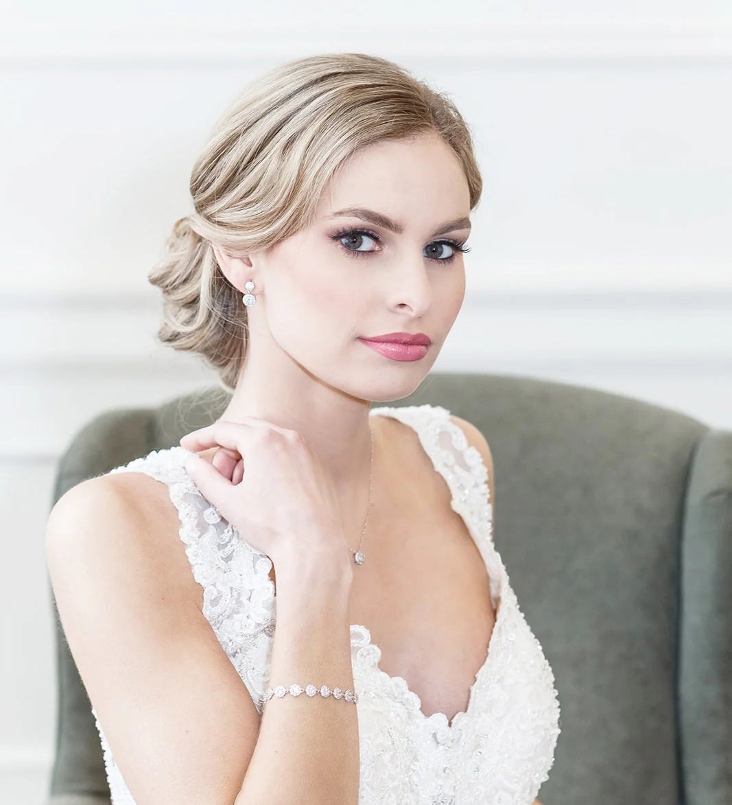 A woman in a white lace wedding dress sits in a chair, her gaze directed off to the side.