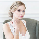 A woman in a white lace wedding dress sits in a chair, her gaze directed off to the side.