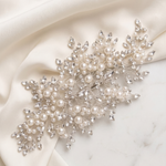 a delicate and elegant piece of jewelry, adorned with numerous pearls and sparkling crystals, resting on a white fabric surface.