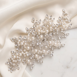 a delicate and elegant piece of jewelry, adorned with numerous pearls and sparkling crystals, resting on a white fabric surface.