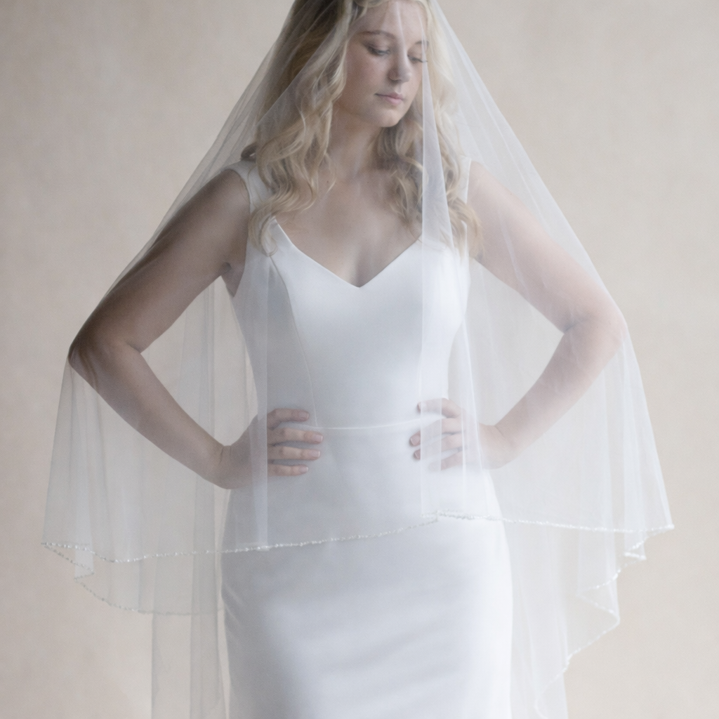 A woman in a white wedding dress stands with her hands on her hips, wearing a veil that covers her face.