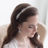 A woman with long brown hair wearing a white lace dress and a decorative headpiece, looking down at her hands.