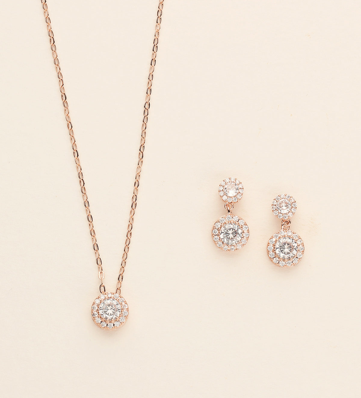 A delicate necklace with a pendant and matching earrings are displayed against a light beige background.