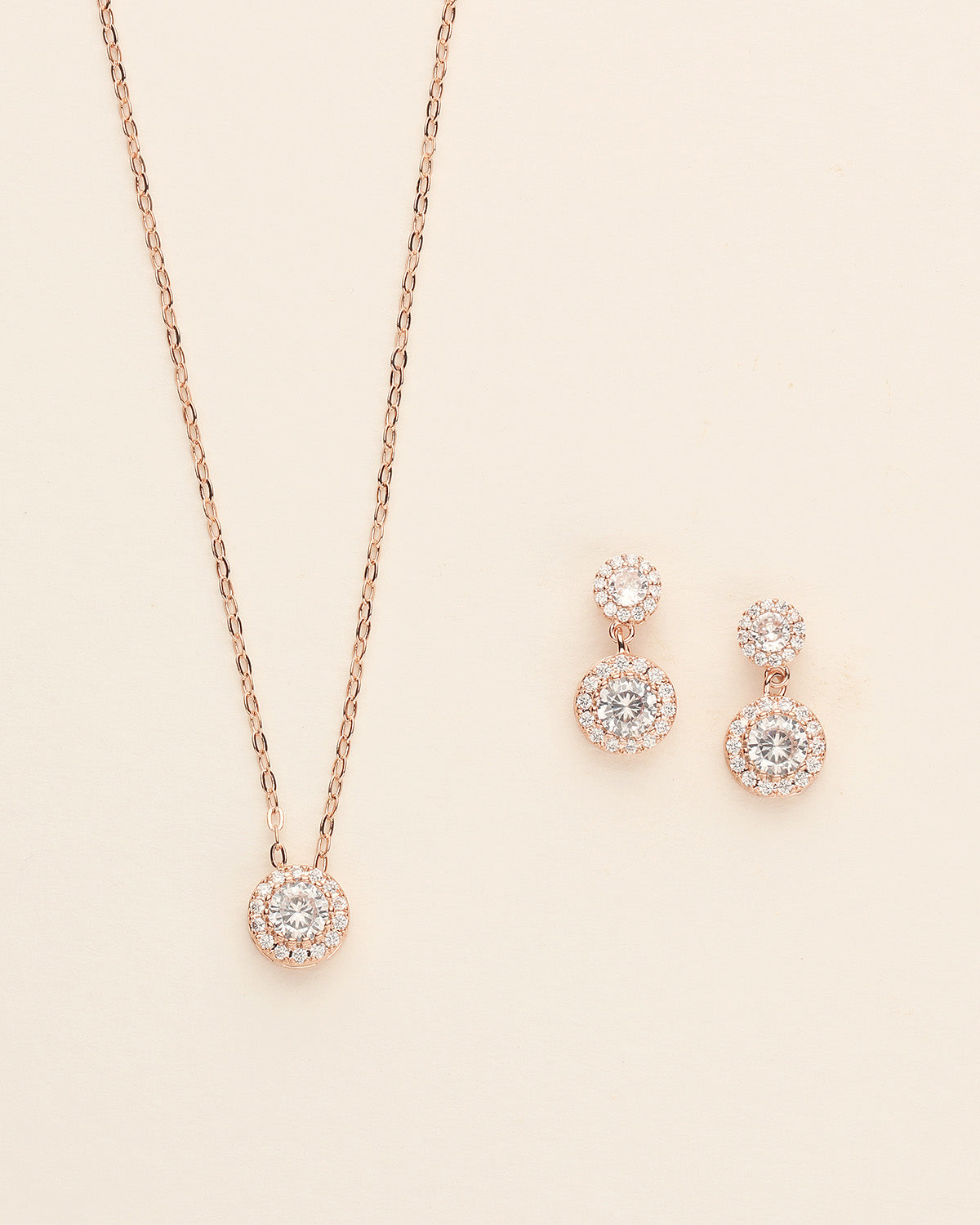 A delicate necklace with a pendant and matching earrings are displayed against a light beige background.