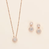 A delicate necklace with a pendant and matching earrings are displayed against a light beige background.