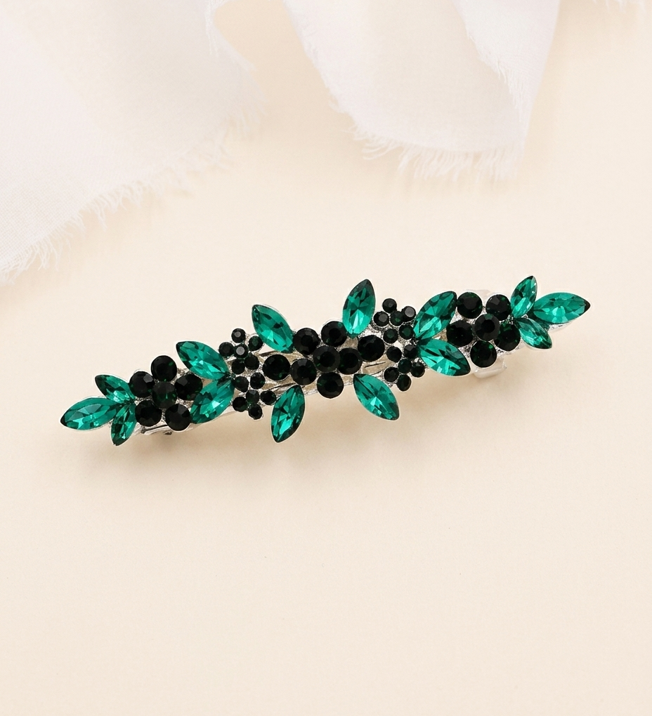 A decorative hair clip with green and black gemstones arranged in a floral pattern.