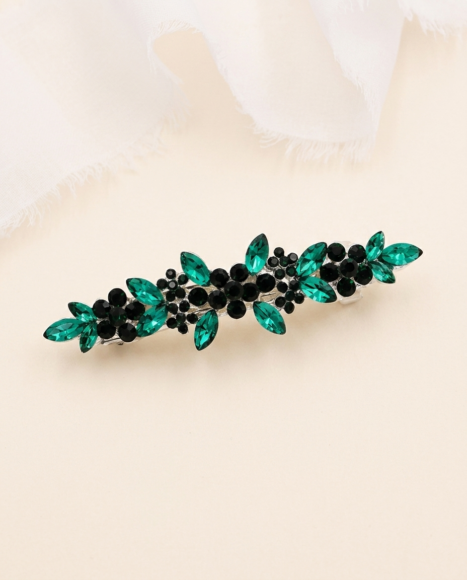 A decorative hair clip with green and black gemstones arranged in a floral pattern.