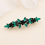 A decorative hair clip with green and black gemstones arranged in a floral pattern.