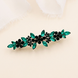 A decorative hair clip with green and black gemstones arranged in a floral pattern.