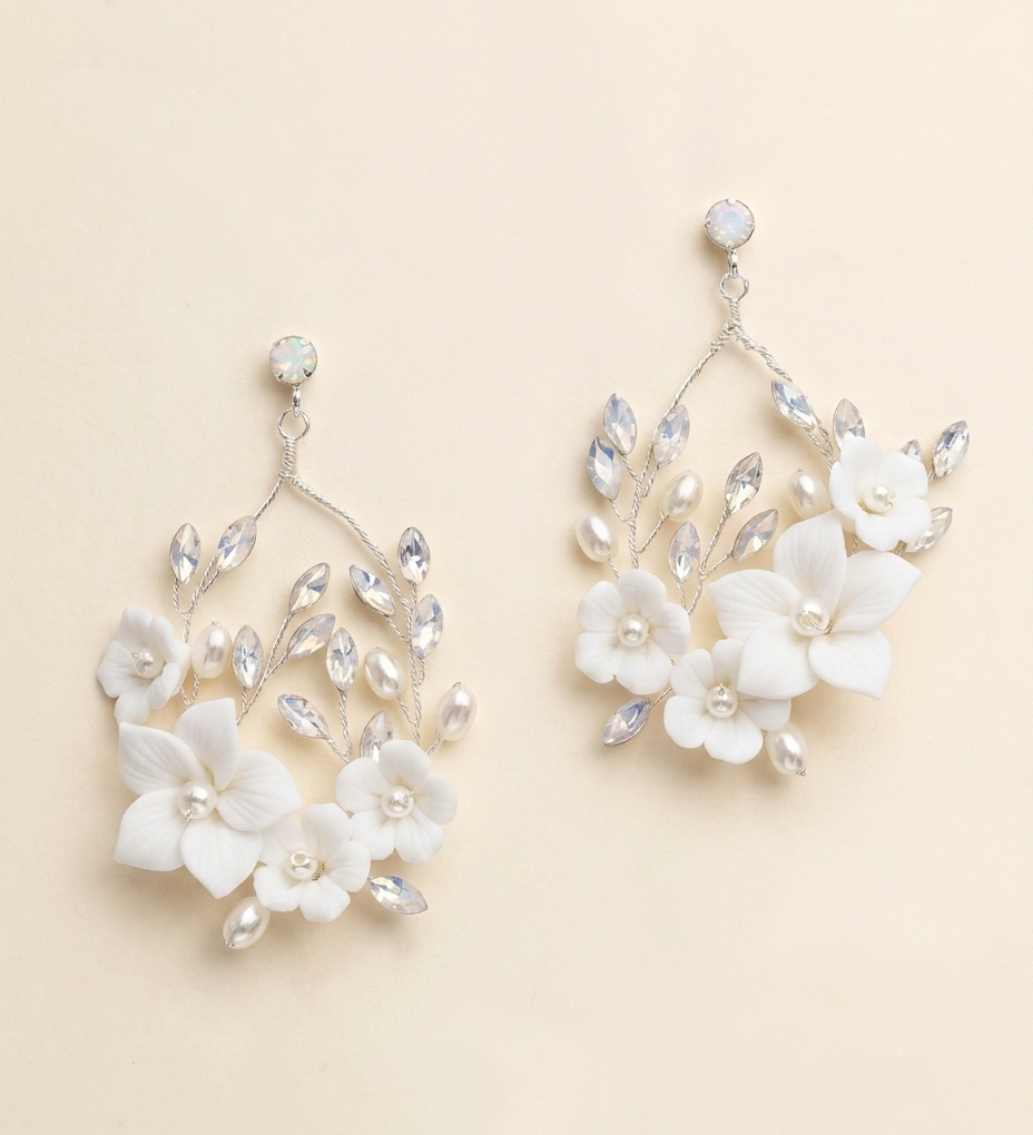 A pair of elegant white floral earrings with crystal accents, displayed against a light beige background.