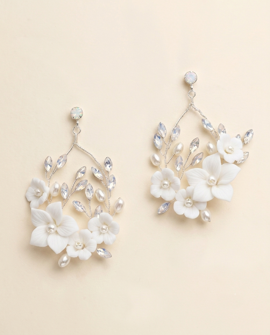 A pair of elegant white floral earrings with crystal accents, displayed against a light beige background.