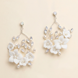 A pair of elegant white floral earrings with crystal accents, displayed against a light beige background.