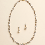A gold necklace and earrings set are displayed against a light beige background.